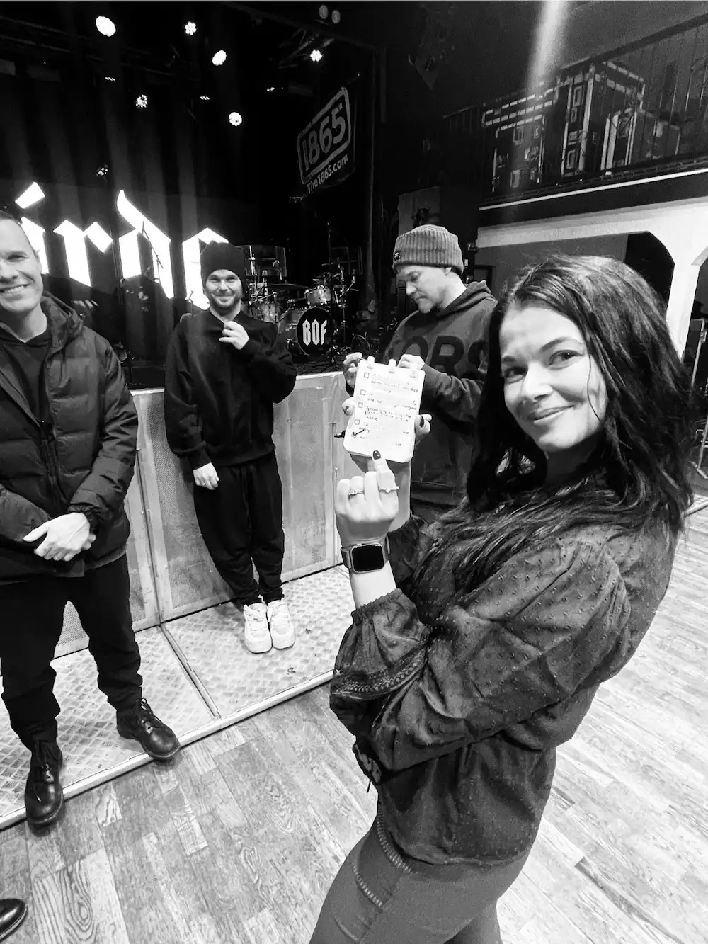 Me posing pointing to a little notebook I have in my hands that has an itemised list in front of the band members.