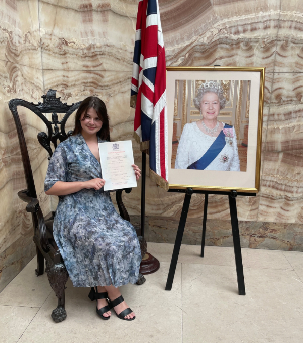 Me holding my naturalisation certificate next to a photo of the Queen.
