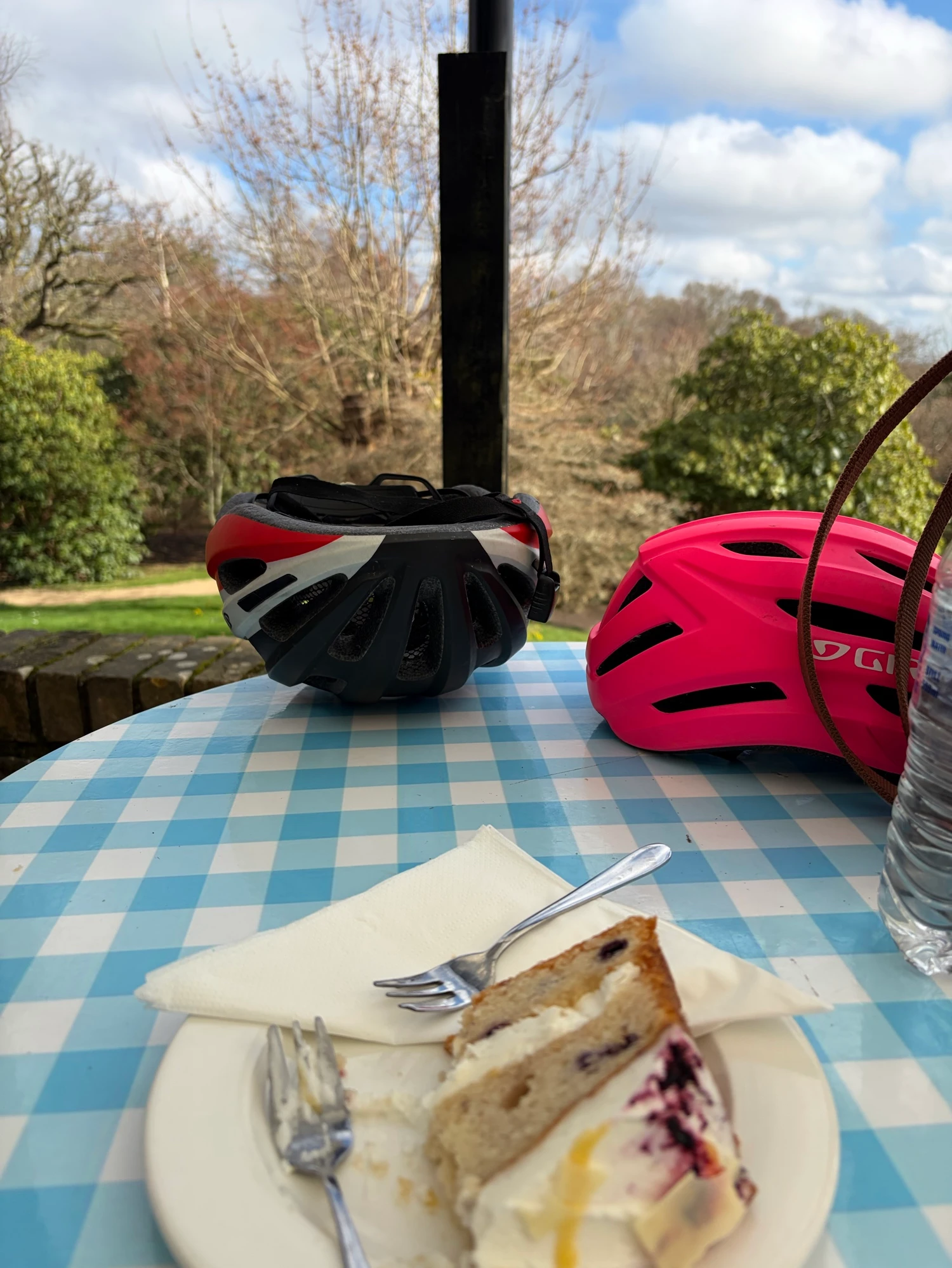 A table overlooking a garden with a slice of cake, water bottle and cycling helmets on top.